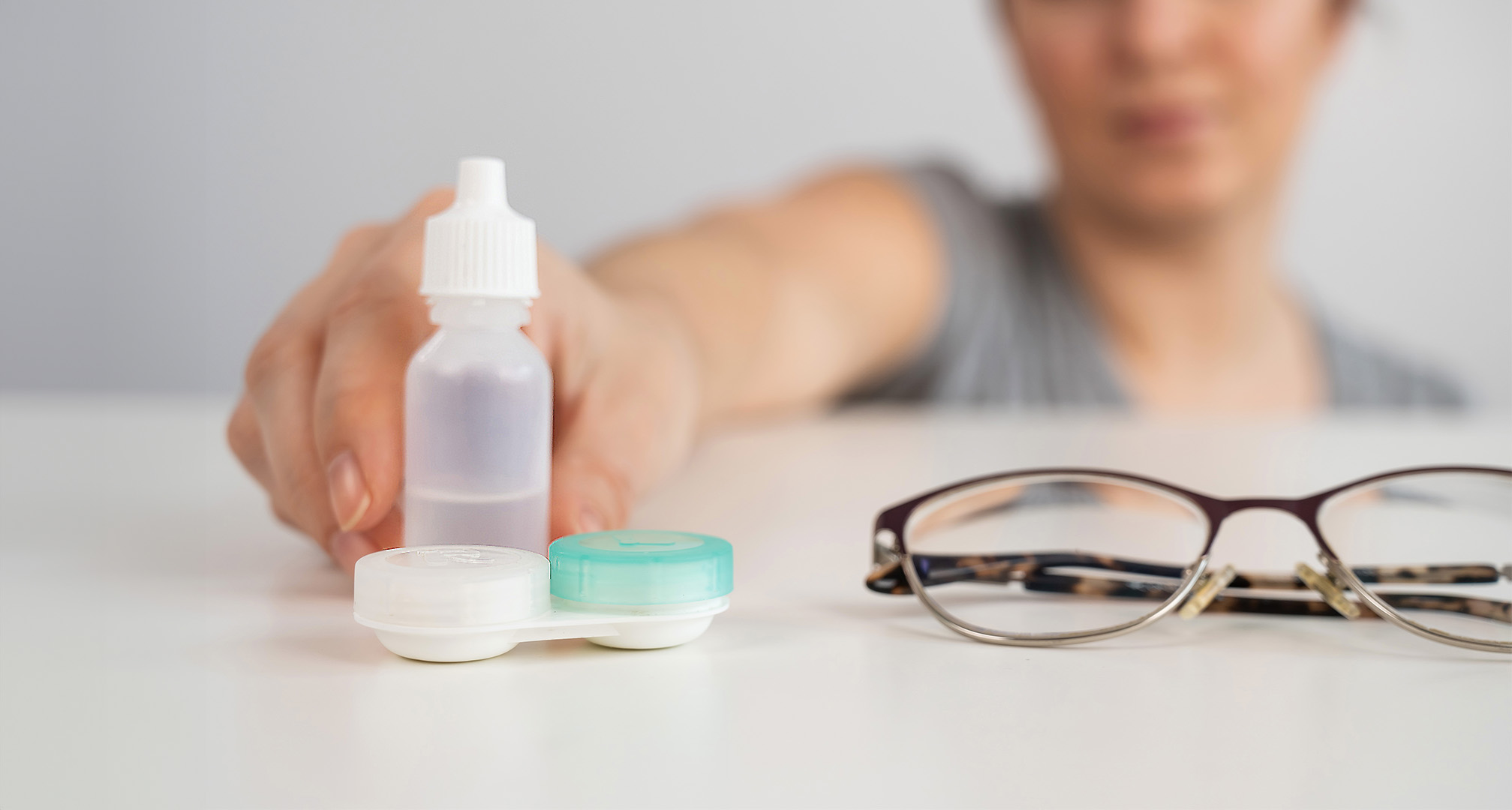 imagen de cerca de gotas para los ojos, estuche de lentes de contacto y gafas sobre una mesa blanca