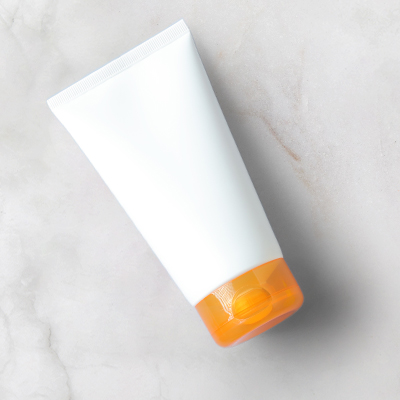 tubo blanco de crema solar con tapón naranja sobre fondo neutro